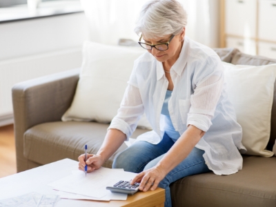 Woman writing on paper with one hand and typing on calculator with the other