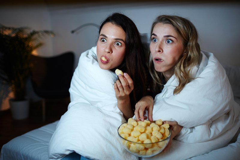 Two women wrapped in a blanket watching a scary movie